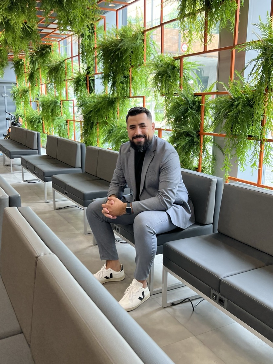 Felipe Cardoso sentado, vestindo um terno cinza, em ambiente com plantas
